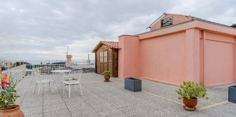 A rooftop terrace with outdoor seating beside a pink building.