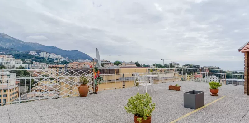 A rooftop terrace overlooks surrounding buildings and a mountain beneath a cloudy sky.