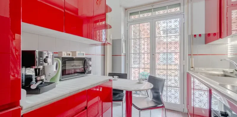 A bright kitchen with red cabinets, appliances, and a small dining table.