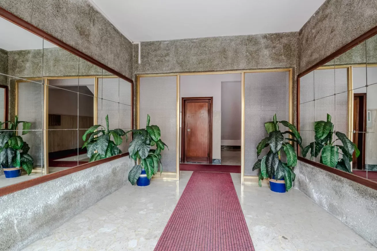 A hallway with mirrored walls, potted plants, and a red runner.