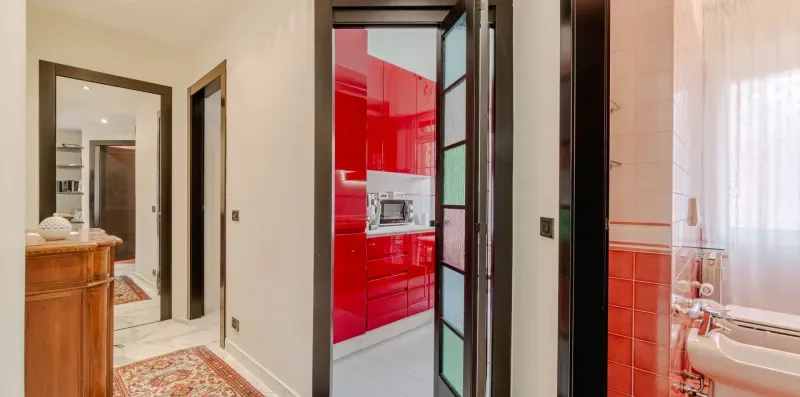 A hallway opens onto a bright red kitchen and a tiled bathroom.