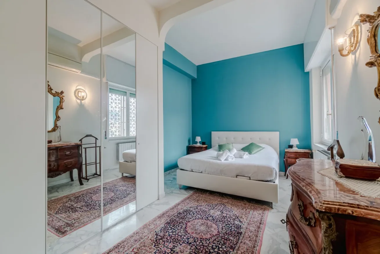 A bedroom with a bed against a teal wall and mirrored closet doors.