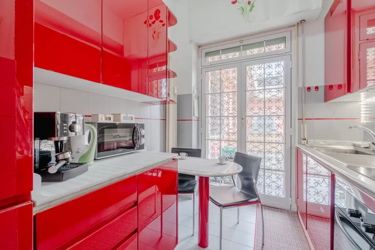 A bright kitchen with red cabinets, countertop appliances, and a small dining table.