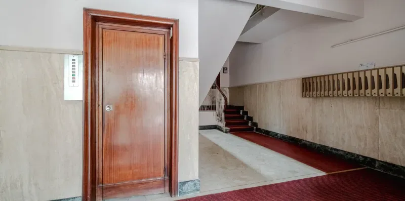 An interior hallway with a wooden door beside a staircase.