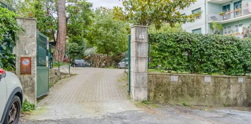 A paved driveway entrance is framed by stone pillars and greenery.