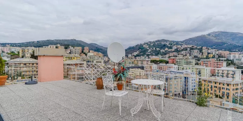 A rooftop terrace overlooks a city with hills in the distance.