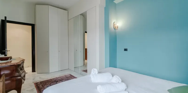 A bedroom with a bed, folded towels, and a mirrored wardrobe.