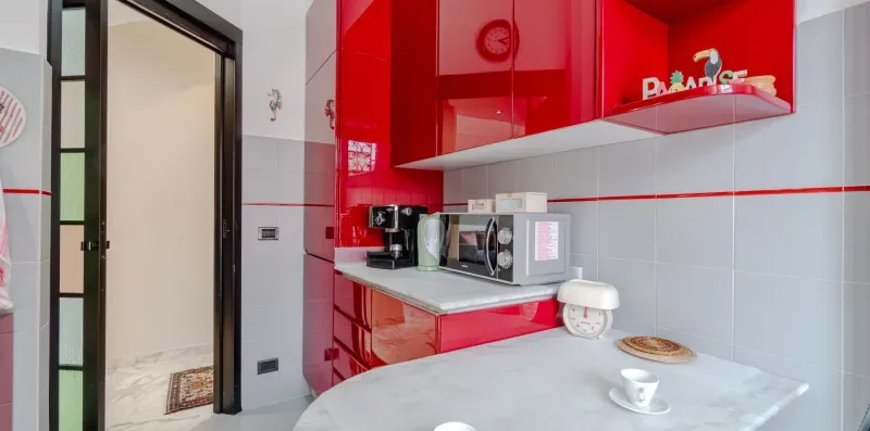A compact kitchen with red cabinets, countertop appliances, and a dining table.