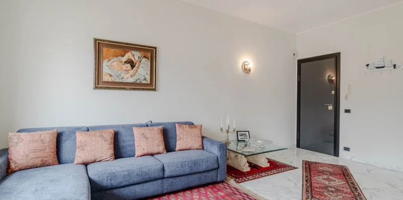 A living room with blue seating, a glass coffee table, and framed wall art.