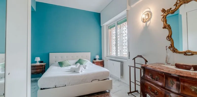 A bedroom with a bed against a turquoise wall and a window beside it.