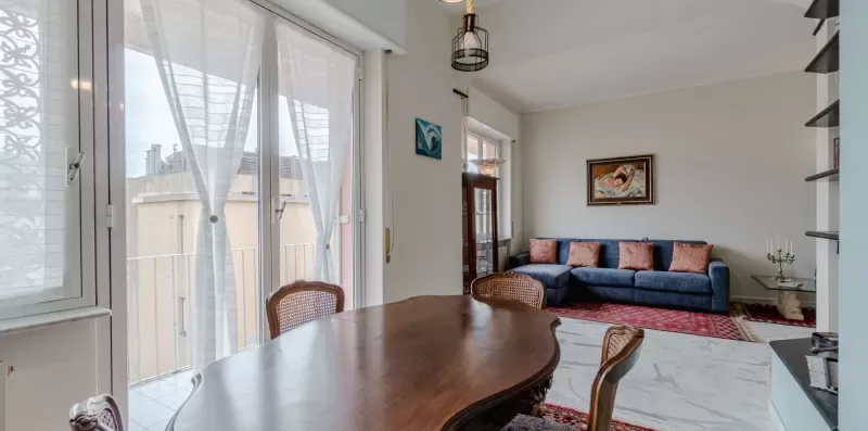 A living room with a blue sofa and a wooden dining table beside large windows.