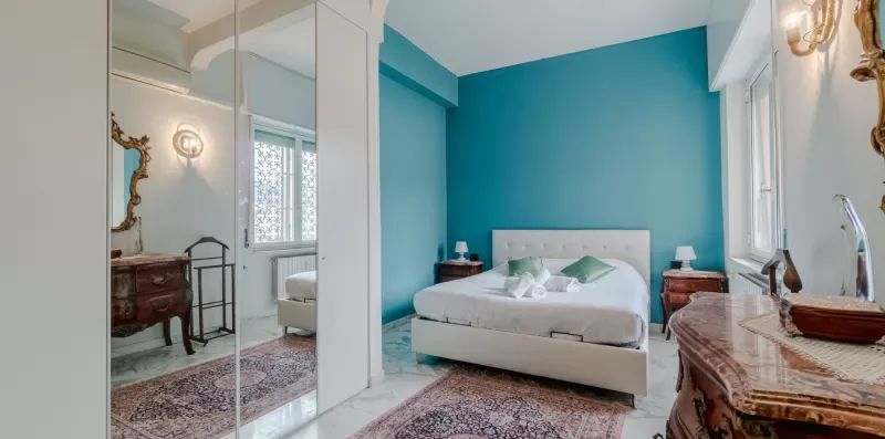 A bedroom with a bed, teal accent wall, and mirrored wardrobe.