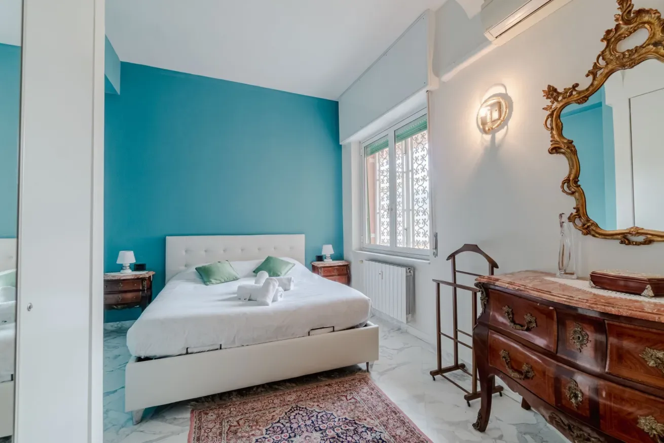 A bedroom with a white bed, turquoise wall, and wooden dresser.