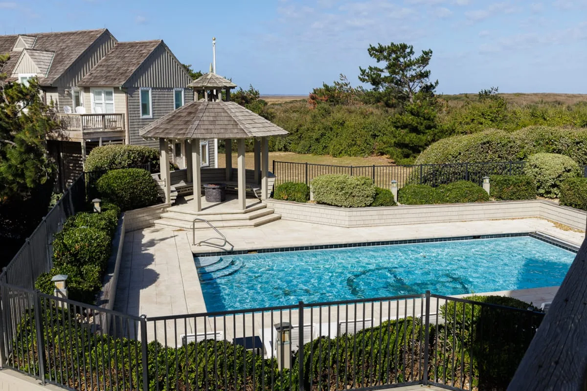 An outdoor swimming pool sits beside a gazebo and landscaped shrubs.