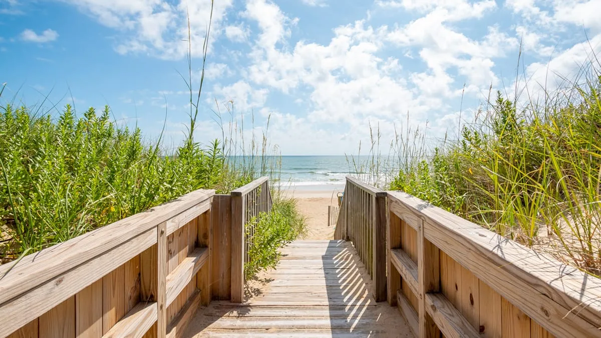 A wooden walkway passes through beach grass toward the ocean.