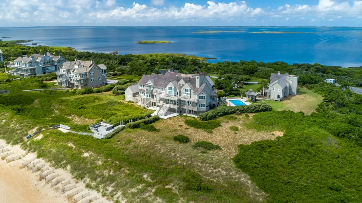 Coastal homes sit among green dunes beside a blue ocean.