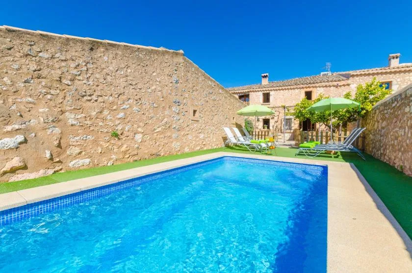 An outdoor swimming pool beside stone walls and shaded seating.