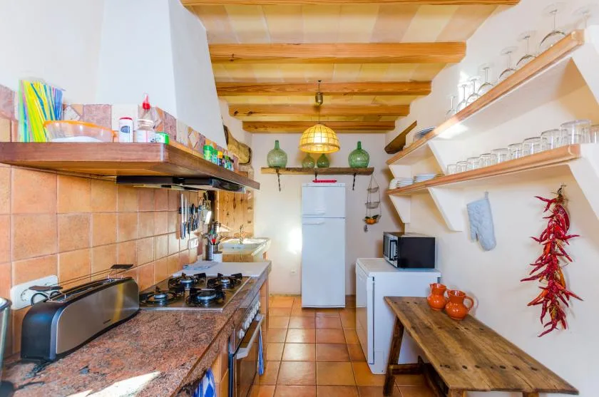 Una cocina rústica con encimeras de azulejos, estantes de madera y una mesa larga.