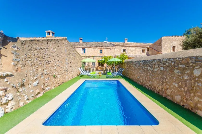 Una piscina está entre muros de piedra junto a un edificio soleado.
