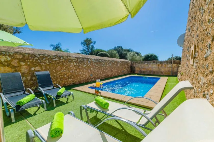 Un patio soleado con tumbonas junto a una piscina rectangular.