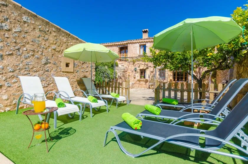 An outdoor seating area with lounge chairs, green umbrellas, and a stone house.