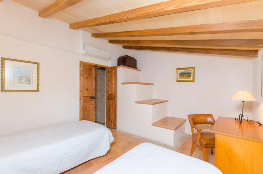 Un dormitorio luminoso con camas, un escritorio y escalones empotrados junto a la pared.