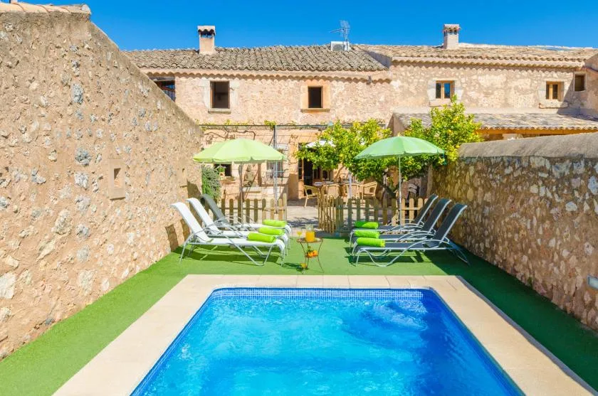 Una piscina al aire libre junto a una terraza con asientos reclinables y sombrillas.