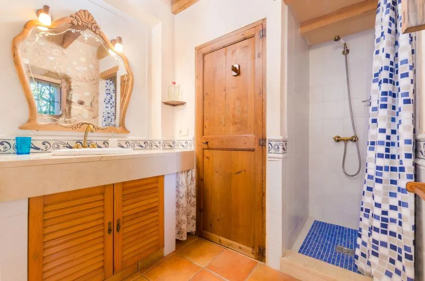 Un baño con tocador de madera, espejo decorativo y zona de ducha con azulejos.