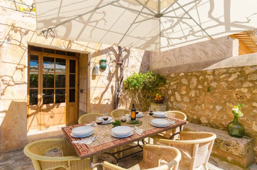 Un comedor exterior iluminado por el sol, con una mesa puesta bajo una gran sombrilla.
