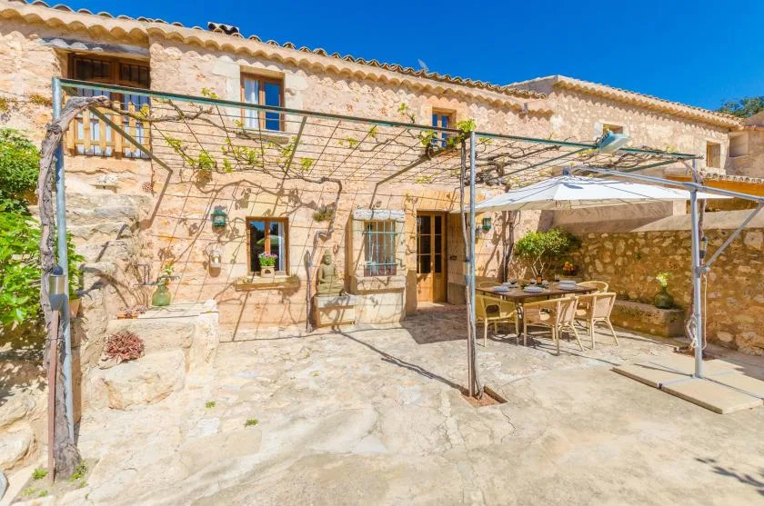 Un patio de piedra con una zona de comedor exterior a la sombra junto a la casa.