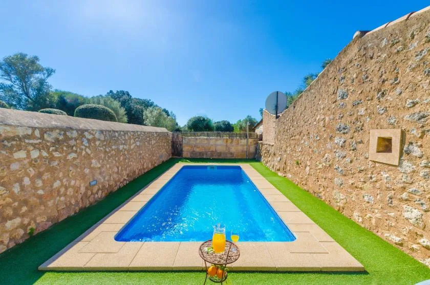 Una piscina está entre muros de piedra, con una mesita en el extremo más cercano.