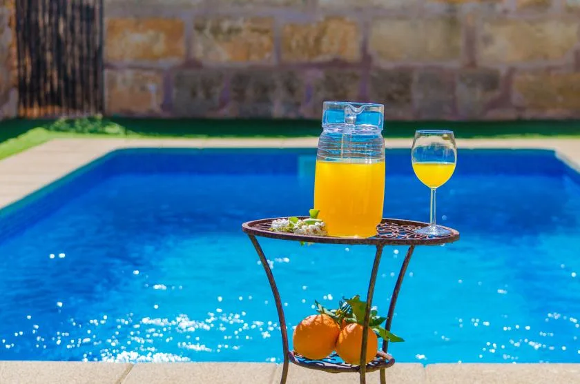 Una piscina con una mesa pequeña que sostiene una jarra y un vaso de jugo de naranja.