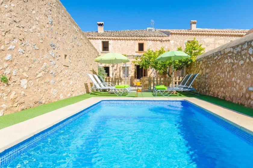 Una piscina ocupa un patio con muros de piedra, con asientos y sombrillas al fondo.