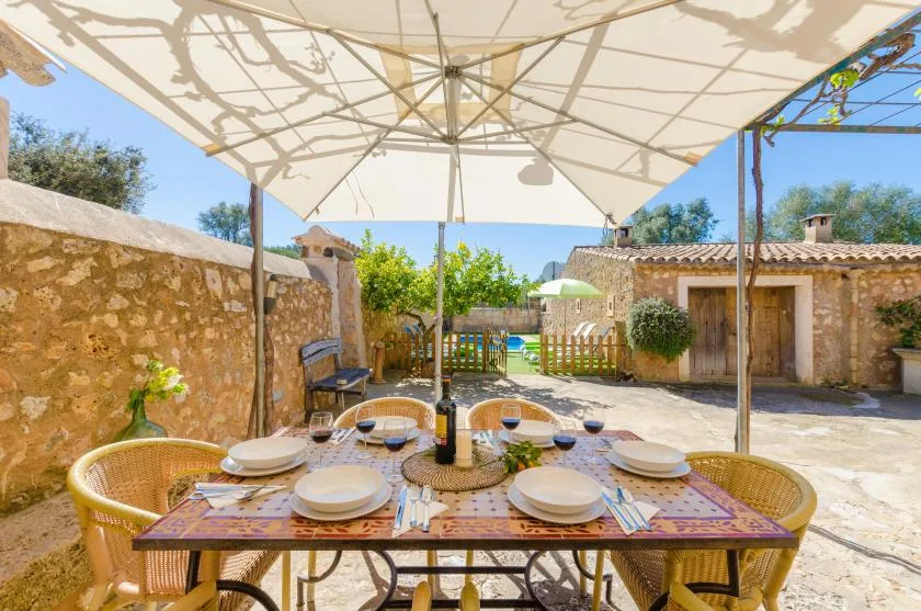 Una zona de comedor al aire libre bajo una sombrilla grande, con un patio y una piscina al fondo.