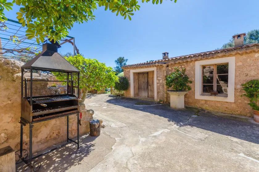 Un patio de piedra con una barbacoa cubierta junto a un edificio de una planta.