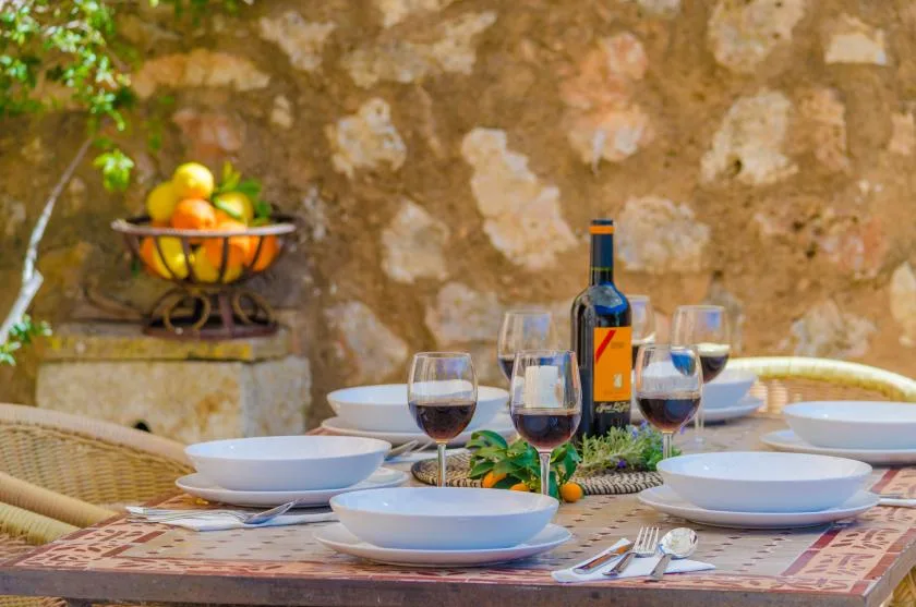 Una mesa está puesta con platos, copas de vino y una botella frente a una pared de piedra.