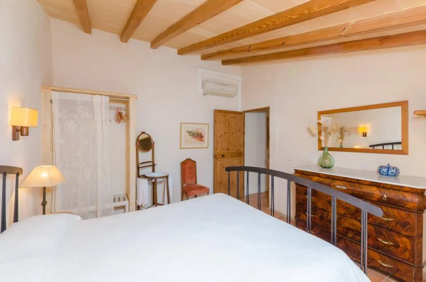 Un dormitorio con una cama, vigas de madera en el techo y una cómoda bajo un espejo.