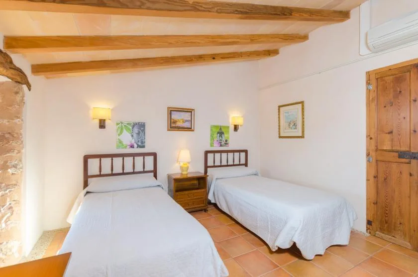 Dormitorio con dos camas individuales, vigas de madera en el techo y suelo de baldosas.