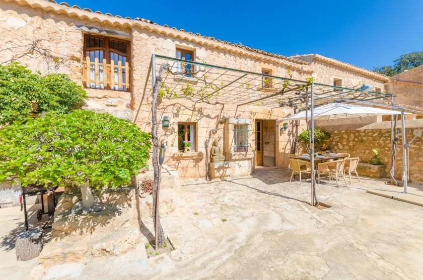 Una casa de piedra da a un patio soleado con una zona de comedor al aire libre a la sombra.