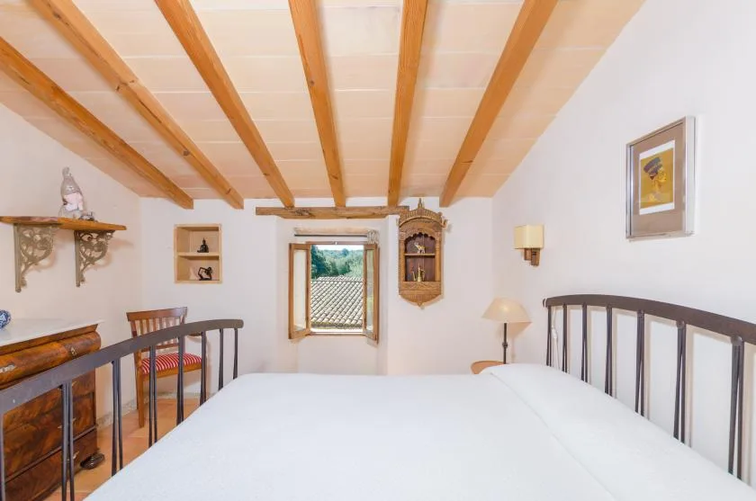 Un dormitorio con una cama grande, vigas de madera en el techo y una ventana con vistas a tejados.