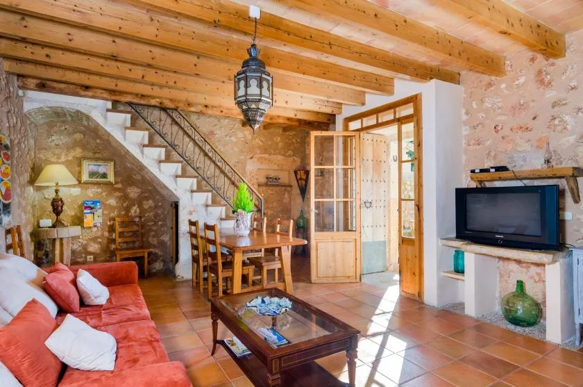 Una sala rústica con mesa de comedor, escalera y televisor.