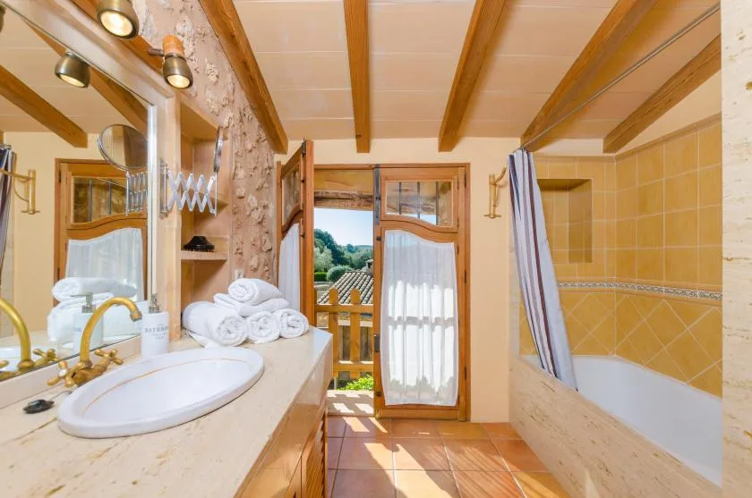 Un baño con lavabo, bañera y puertas abiertas que dan a un balcón.