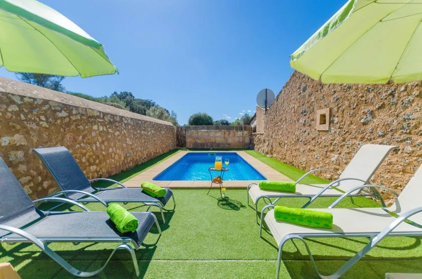 Una pequeña piscina al aire libre está rodeada de asientos, césped artificial y muros de piedra.