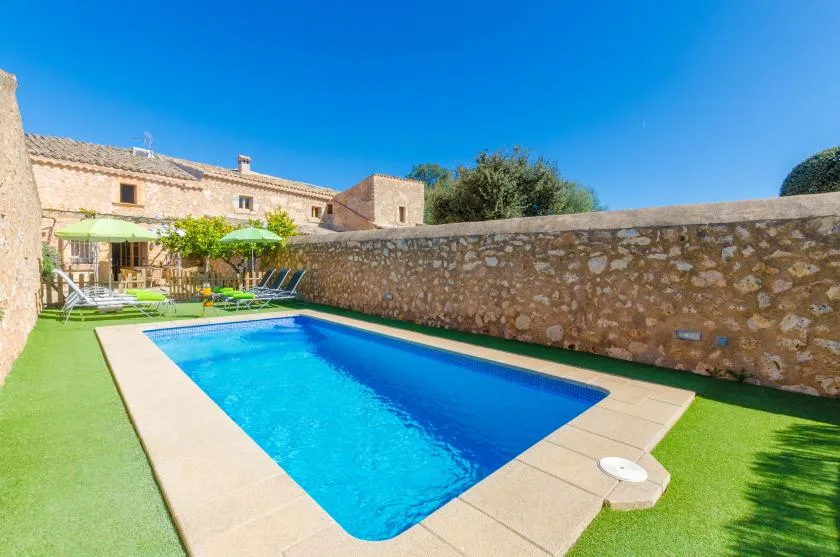 An outdoor swimming pool sits beside a stone wall and grassy lawn.