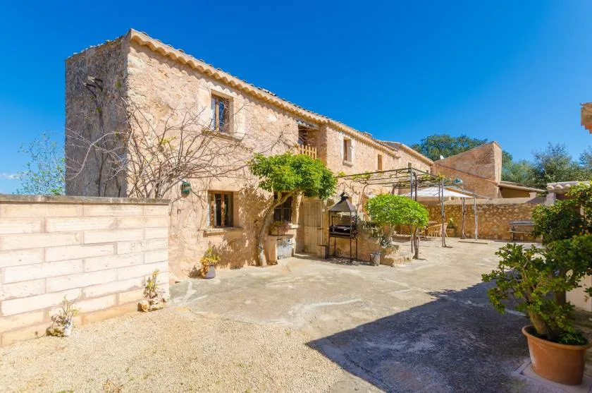 Una casa de piedra da a un patio soleado con una zona de estar al aire libre a la sombra.