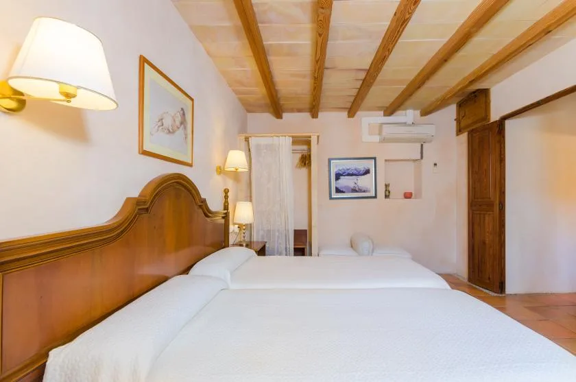 Un dormitorio con ropa de cama blanca, cabecero de madera y vigas expuestas en el techo.