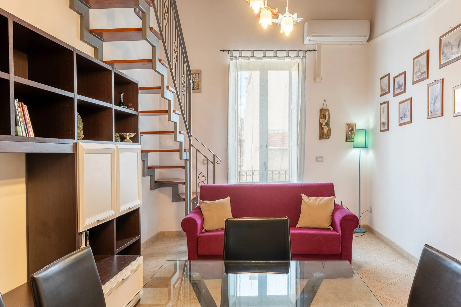 Una sala de estar con un sofá rojo, una mesa de centro de vidrio y una escalera abierta.