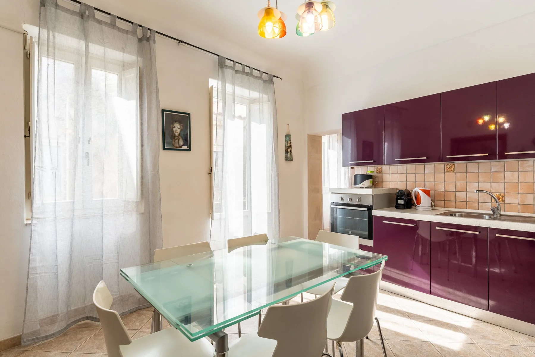 Una cocina luminosa con comedor, mesa de vidrio y gabinetes color ciruela.