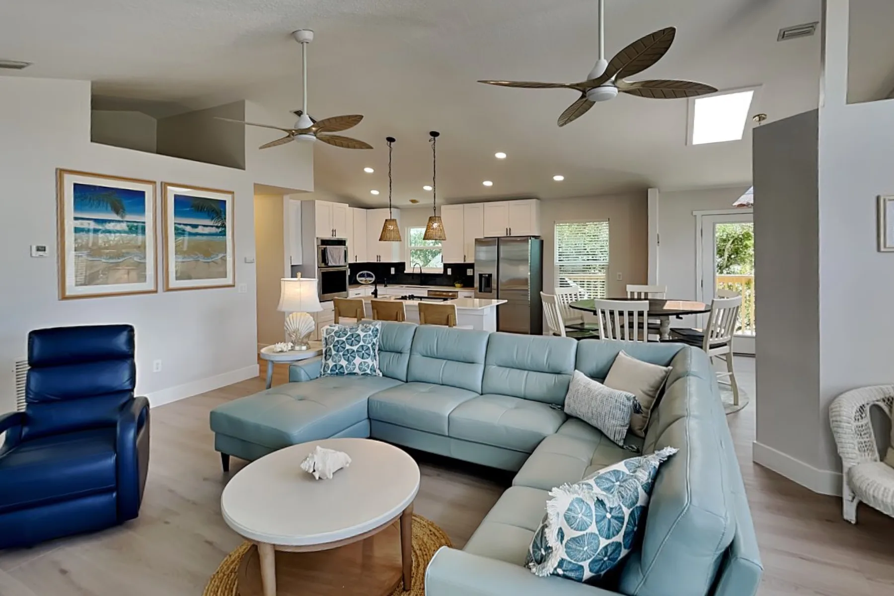 An open-plan living room with a sectional seating area and kitchen behind it.