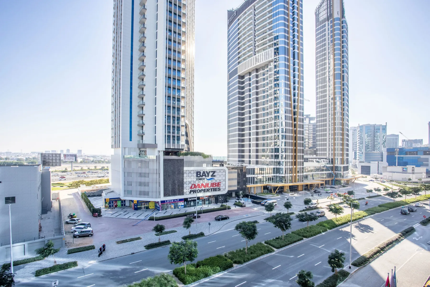 Modern high-rise buildings stand beside a landscaped urban roadway.